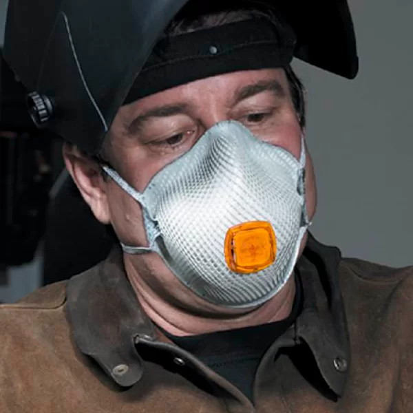 Un trabajador con un casco de soldadura y un respirador protector plateado con un filtro naranja en el frente. su atención parece dirigida hacia abajo, probablemente en su trabajo, en un taller.