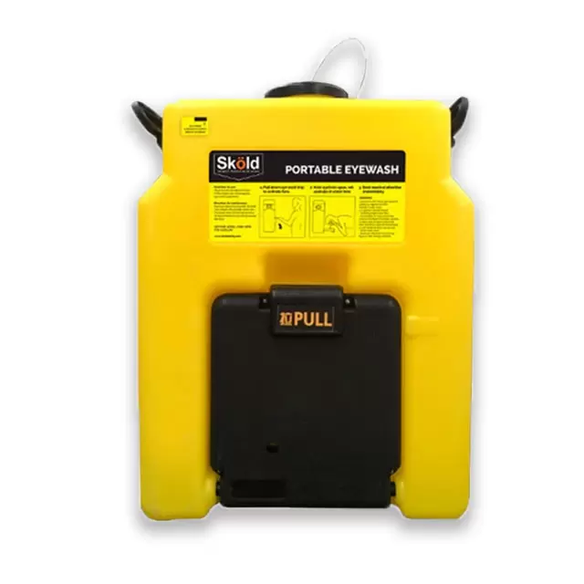 Una estación portátil de lavado de ojos de color amarillo con la marca "sköld" en la parte superior. Cuenta con diagramas de instrucciones y texto, con una palanca negra prominente en la parte inferior para su operación.
