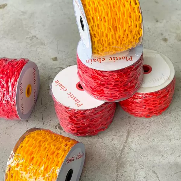 Pilas de coloridas cadenas de plástico en rojo y amarillo, algunas enrolladas en carretes, con etiquetas hacia arriba que dicen "cadena de plástico". el fondo es una superficie gris texturizada.