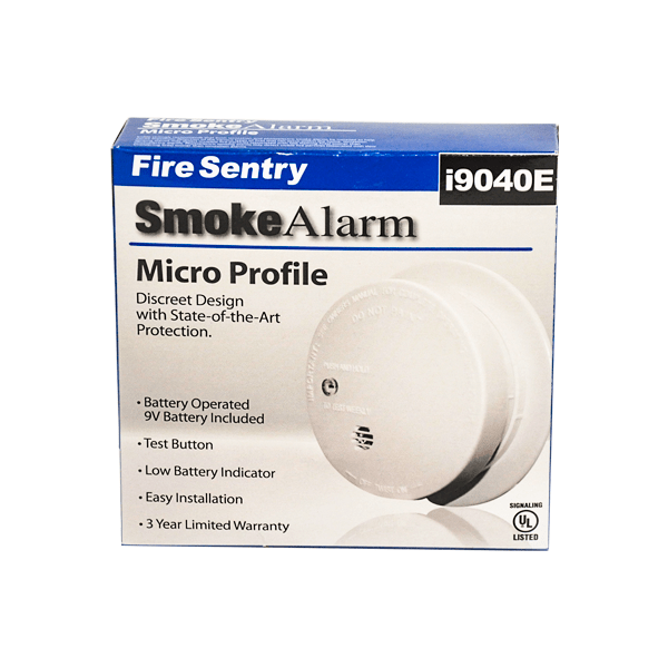 Una alarma de humo Fire Sentry i9040e en su embalaje. la caja es azul y blanca y detalla características como "protección de última generación" y "fácil instalación". la alarma de humo cilíndrica de color blanco es visible en el lado derecho.