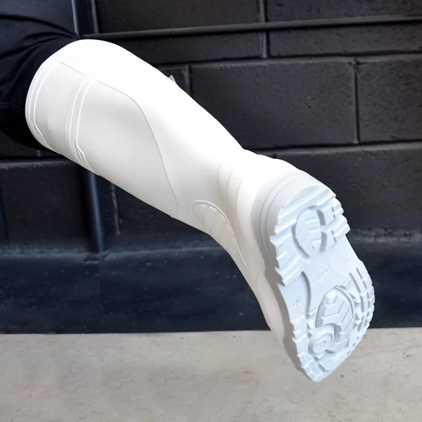 Un primer plano de una pierna protésica que presenta un diseño moderno y estilizado con una capa exterior blanca y una suela con dibujo, sobre un fondo de pared de ladrillo oscuro.